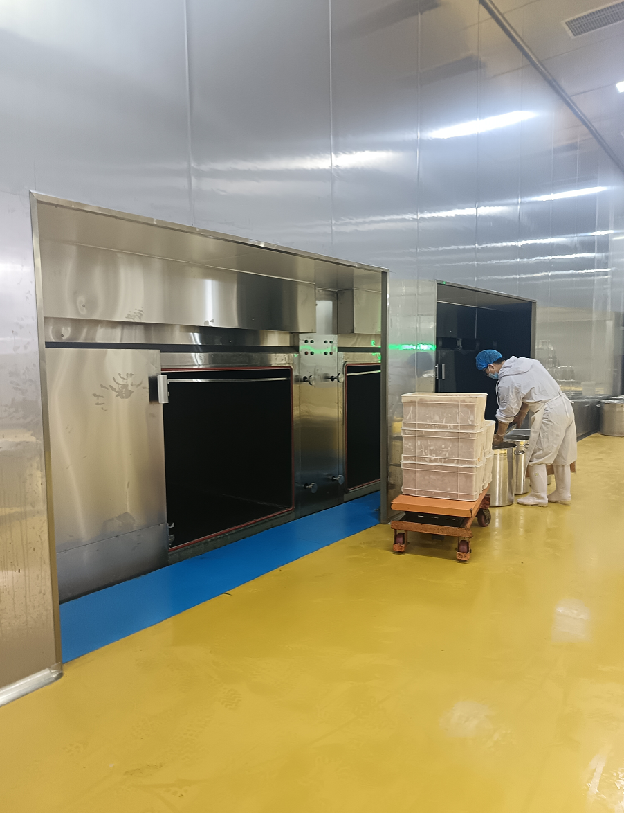 预处理车间进料端：工人正将高温食材推入宽敞的预冷舱内。大昌重型预冷设备容量大、承重强，非普通家用级别，专为高强度、大批量的工业连续生产而生。